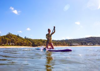 Woman enjoying a morning stand up paddleboarding, Pearl Beach, Central Coast