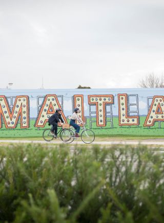 メイトランドのエルギン通りにある「メイトランドへようこそ」の看板の前を自転車で通り過ぎるカップル